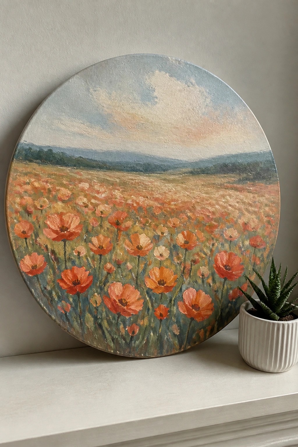 Circular poppy field painting on round canvas beside potted succulent on white ledge.