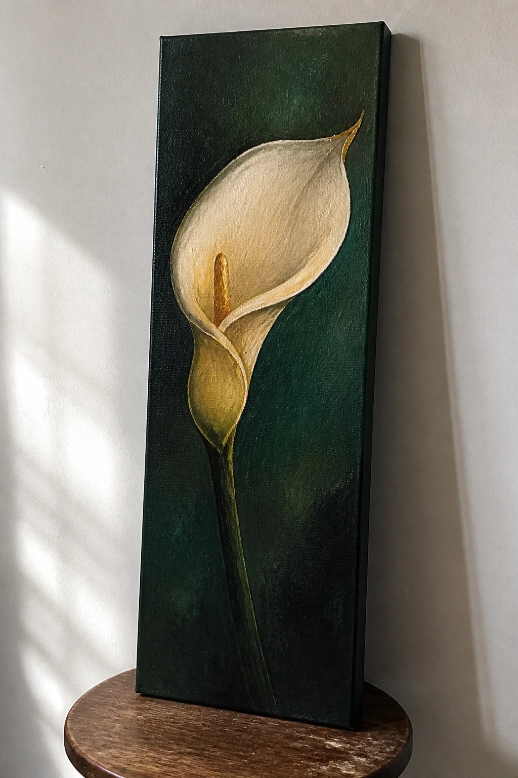 A vertical acrylic painting of a single white calla lily with yellow spadix on a dark green background, shown on a wooden stand.
