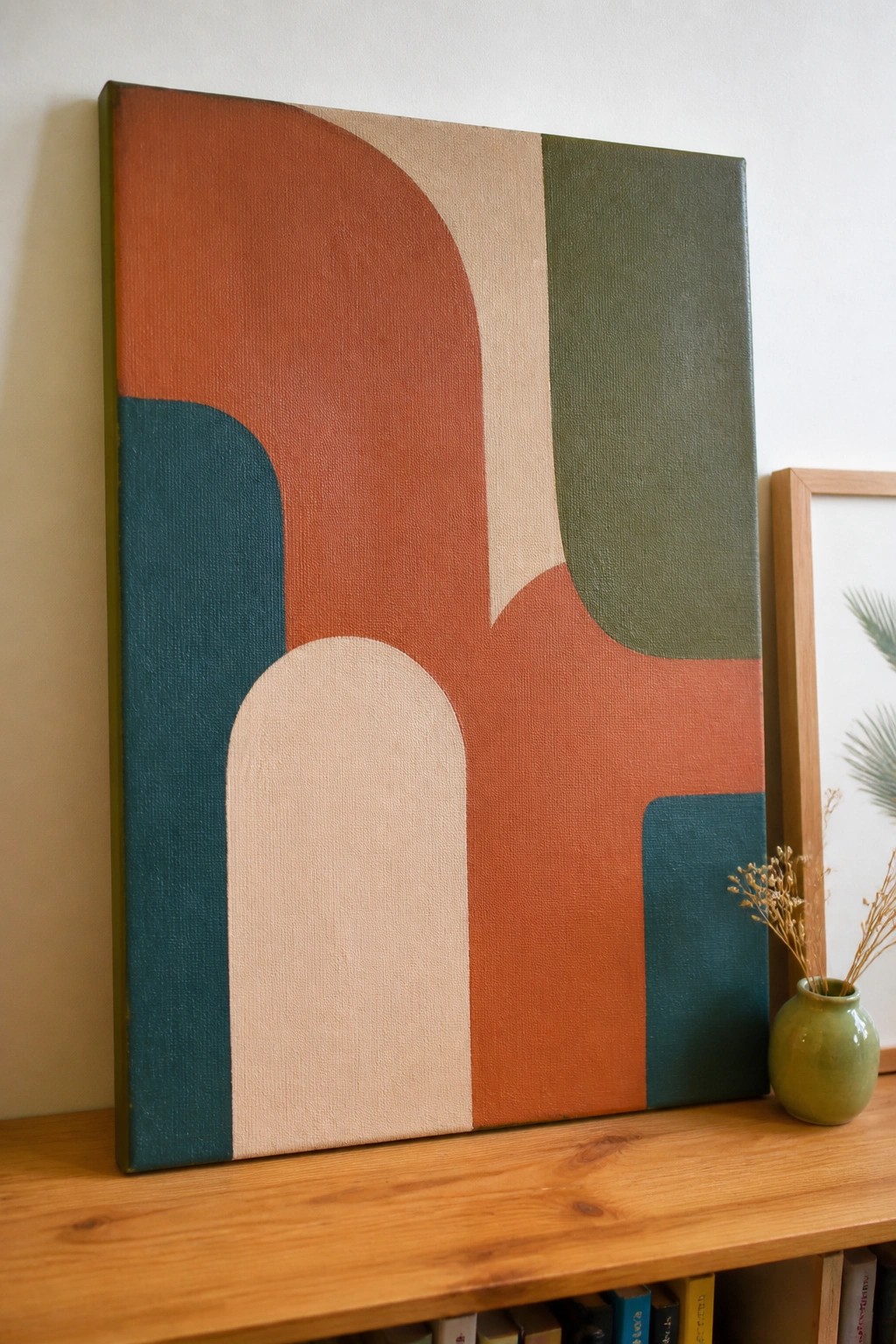 Abstract painting with curved shapes in terracotta, beige, teal, and green beside green vase