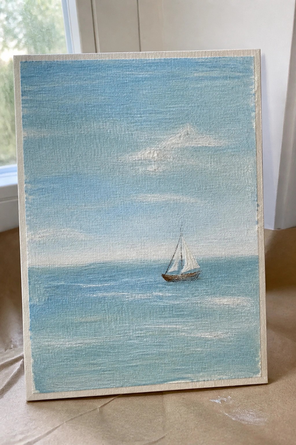 Small sailboat with white sails on calm blue sea under cloudy sky