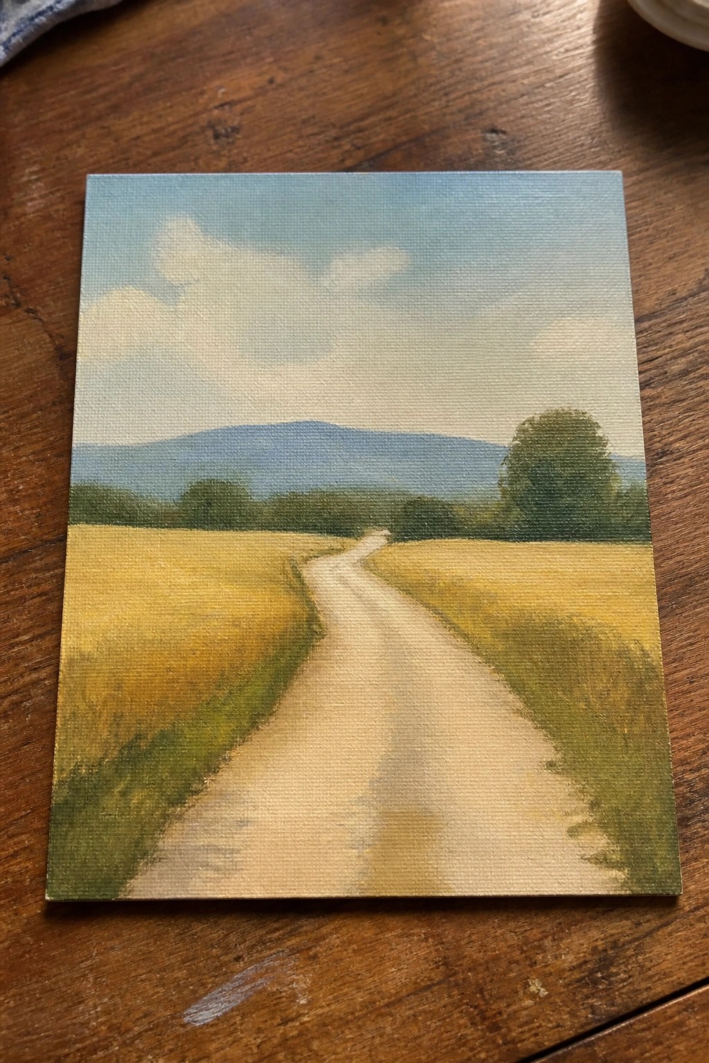 Winding dirt road through golden fields toward blue mountains on wooden table.
