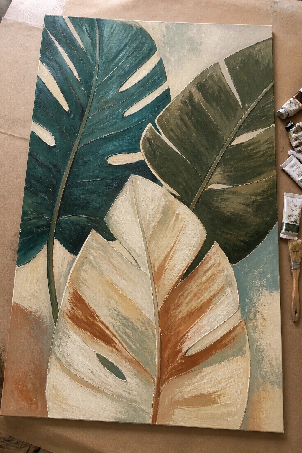 Abstract painting of oversized tropical leaves in teal, green, and brown tones beside paint tubes.