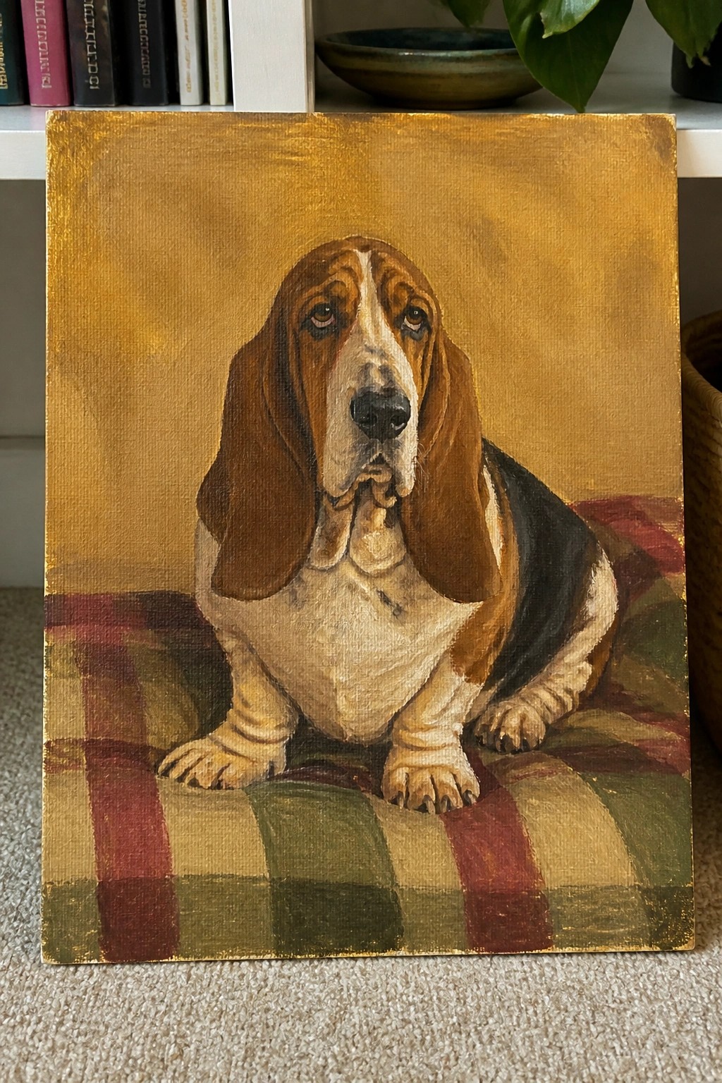 Detailed oil painting of basset hound on colorful plaid cushion with golden background.