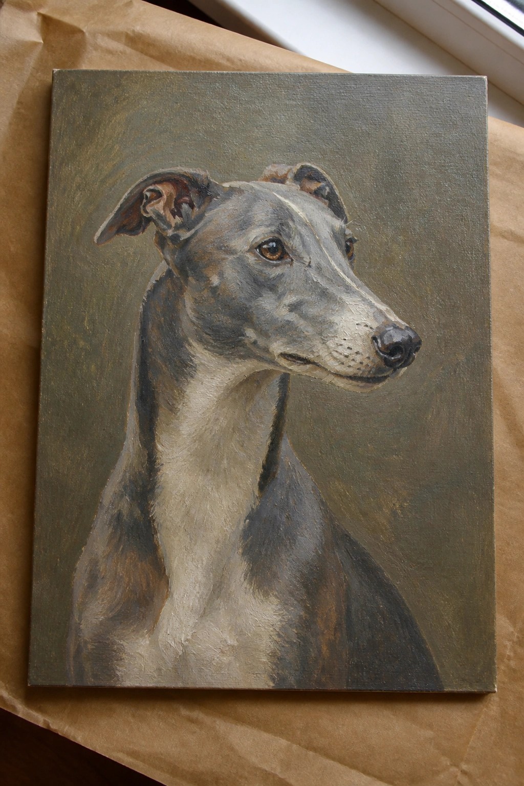 Realistic painting of a greyhound head in profile on canvas over brown paper.