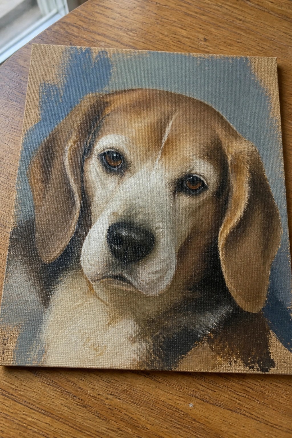 Realistic beagle portrait painting on canvas atop wooden table with blue background