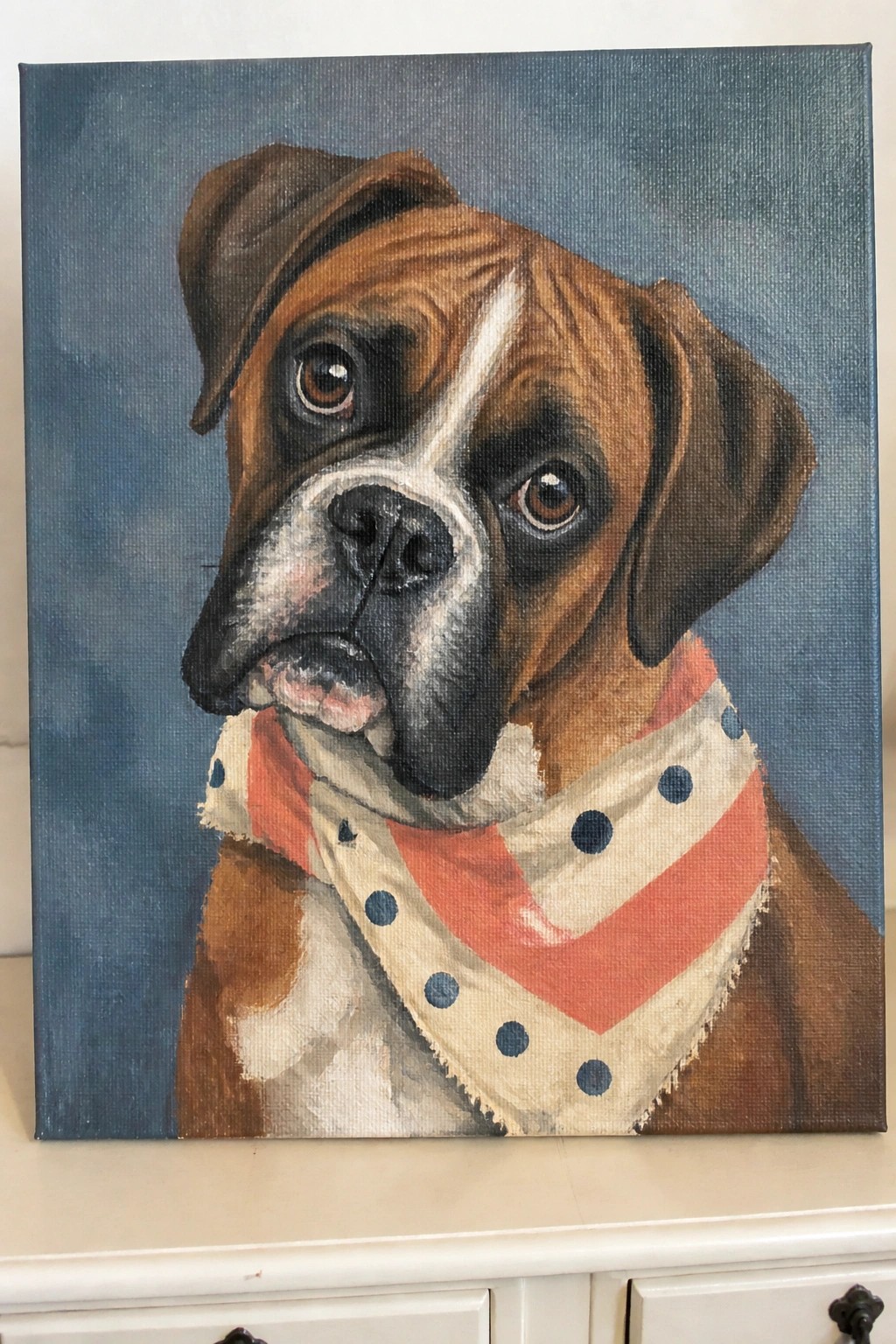 Realistic painting of a boxer dog wearing a red polka-dotted bandana on blue background