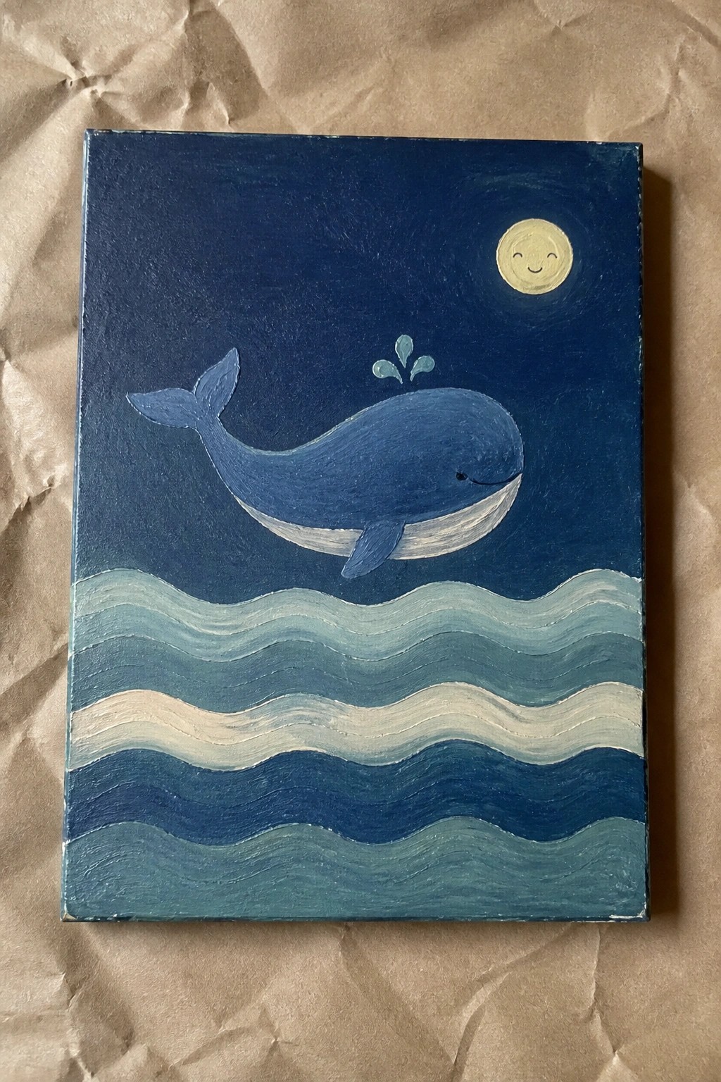 A small oil painting of a blue whale jumping from wavy blue and white water under a smiling yellow moon against a dark blue night sky on brown paper.