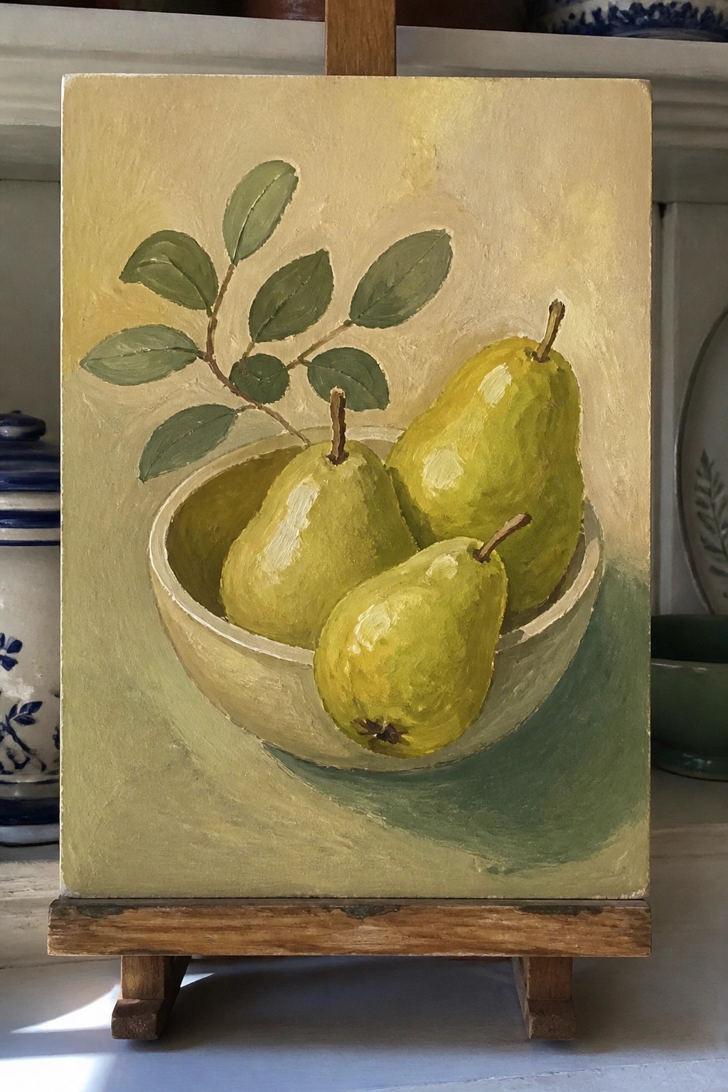 Three green pears in a white bowl with leafy branch on easel.
