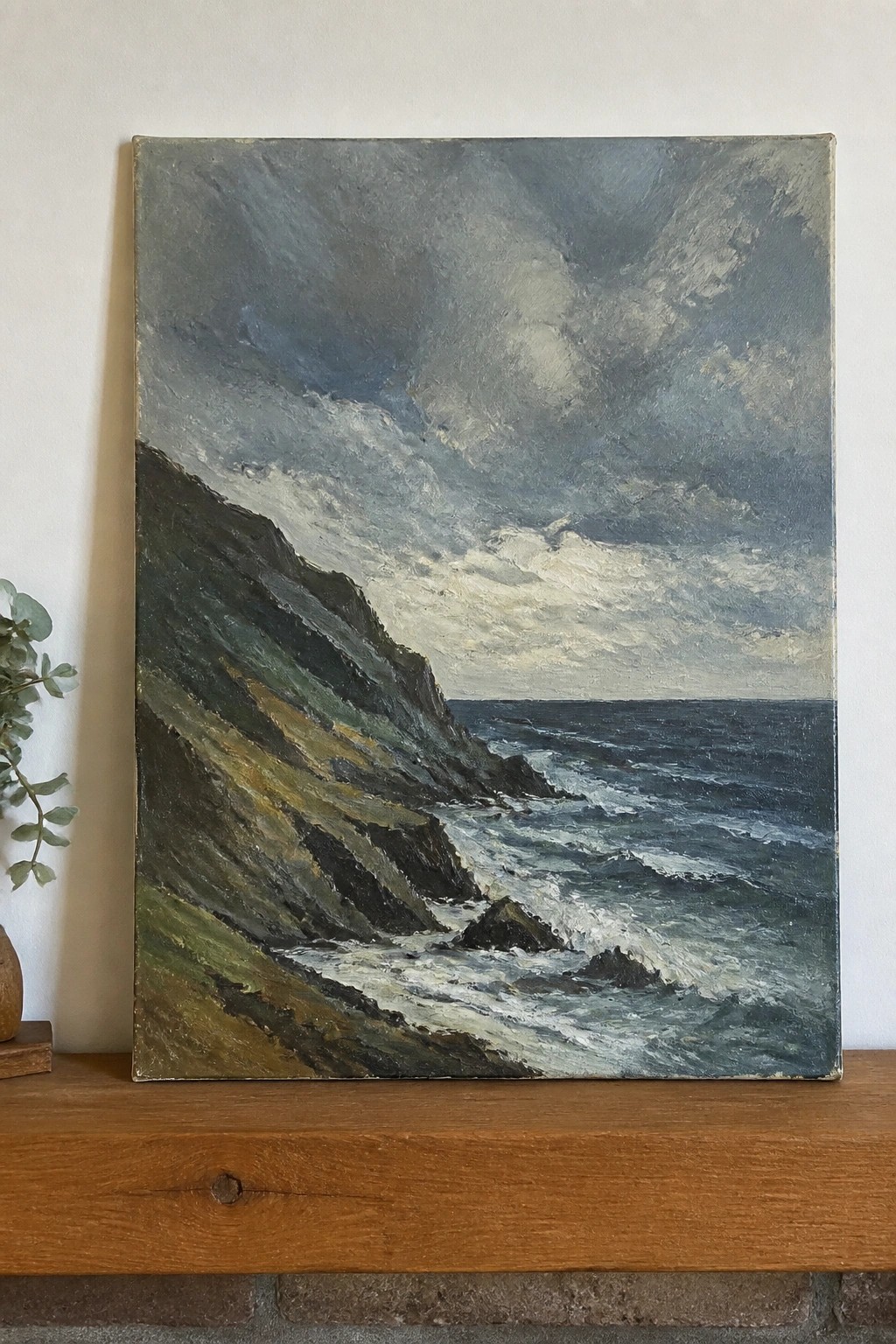 Stormy seascape painting with crashing waves against dark cliffs on wooden shelf.