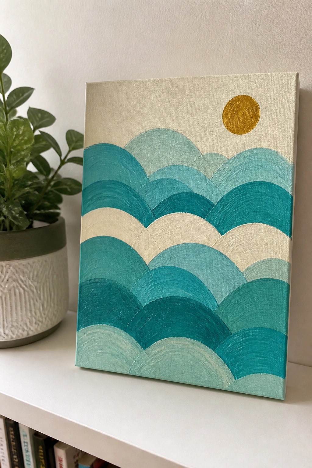 Teal wave painting with gold sun on white shelf beside potted plant.