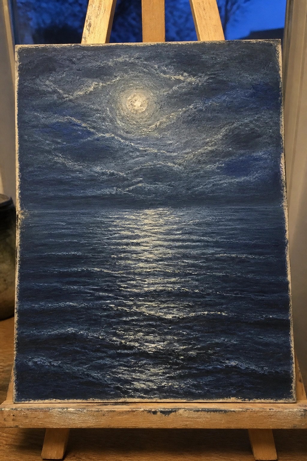 Dark blue seascape painting with full moon and reflection on wooden easel