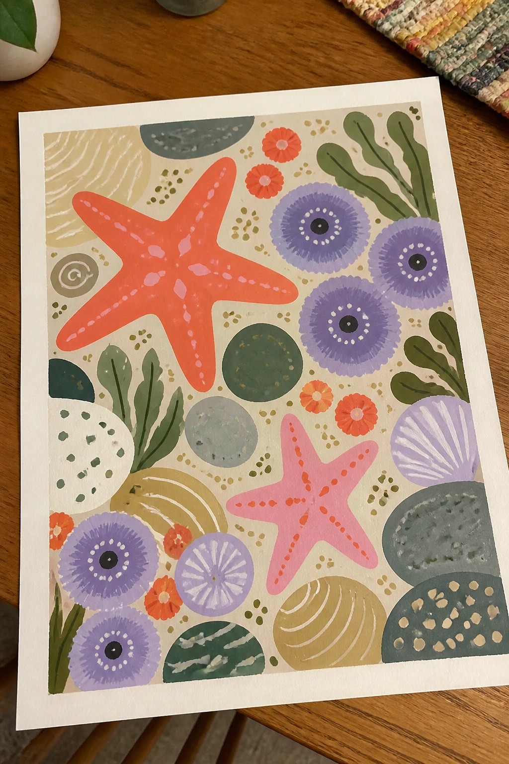 Colorful abstract print with orange starfish, purple blooms, green leaves and seashells on beige background