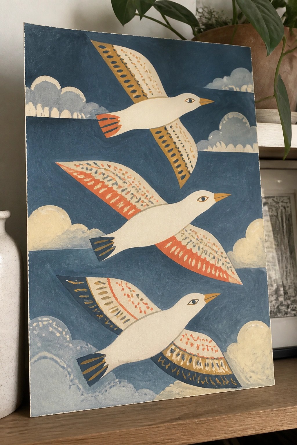 Three stylized white birds with patterned wings soaring over blue waters and clouds.