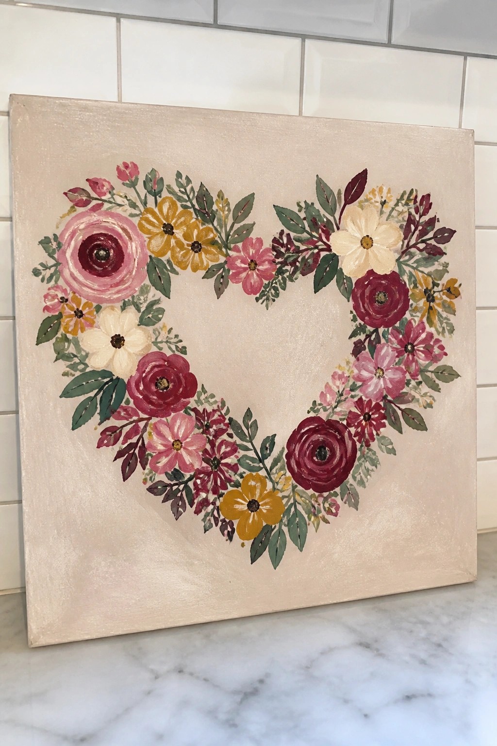 Heart-shaped floral wreath painting in pink, yellow, and burgundy on beige canvas.