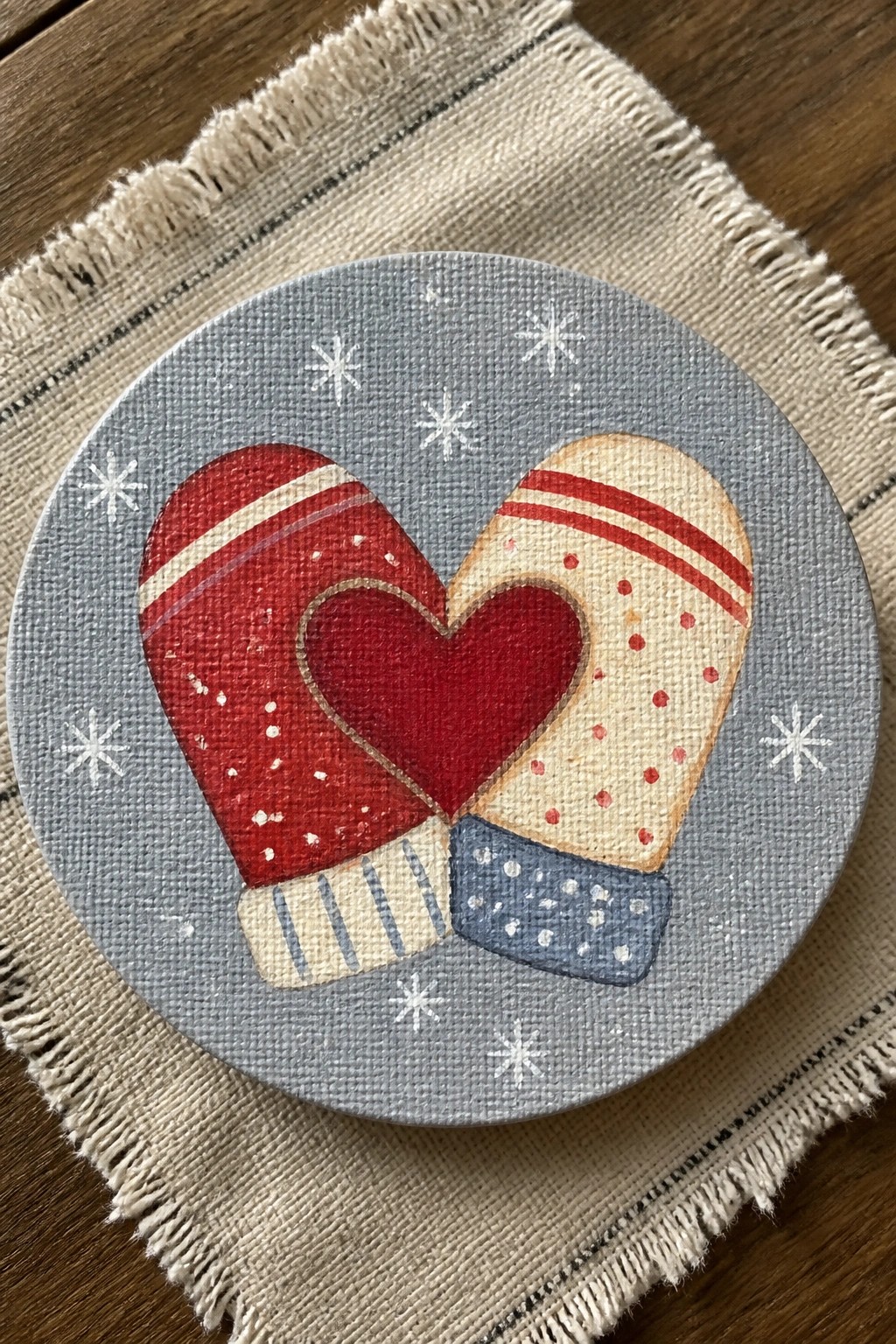 Red and beige mittens forming a heart on gray canvas with white snowflakes