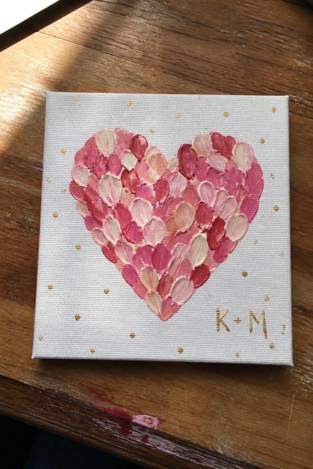 Pink heart of layered brushstrokes with gold dots and K+M on canvas