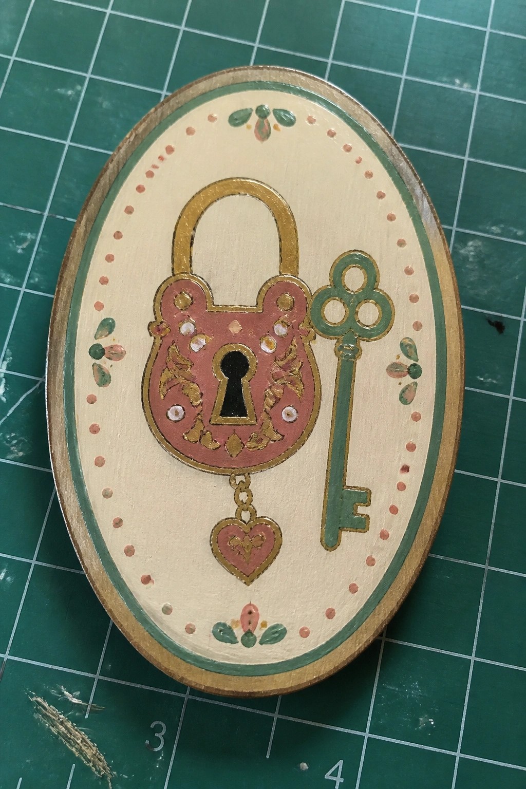 Oval wooden plaque with pink padlock, green key, dangling heart, and floral designs.