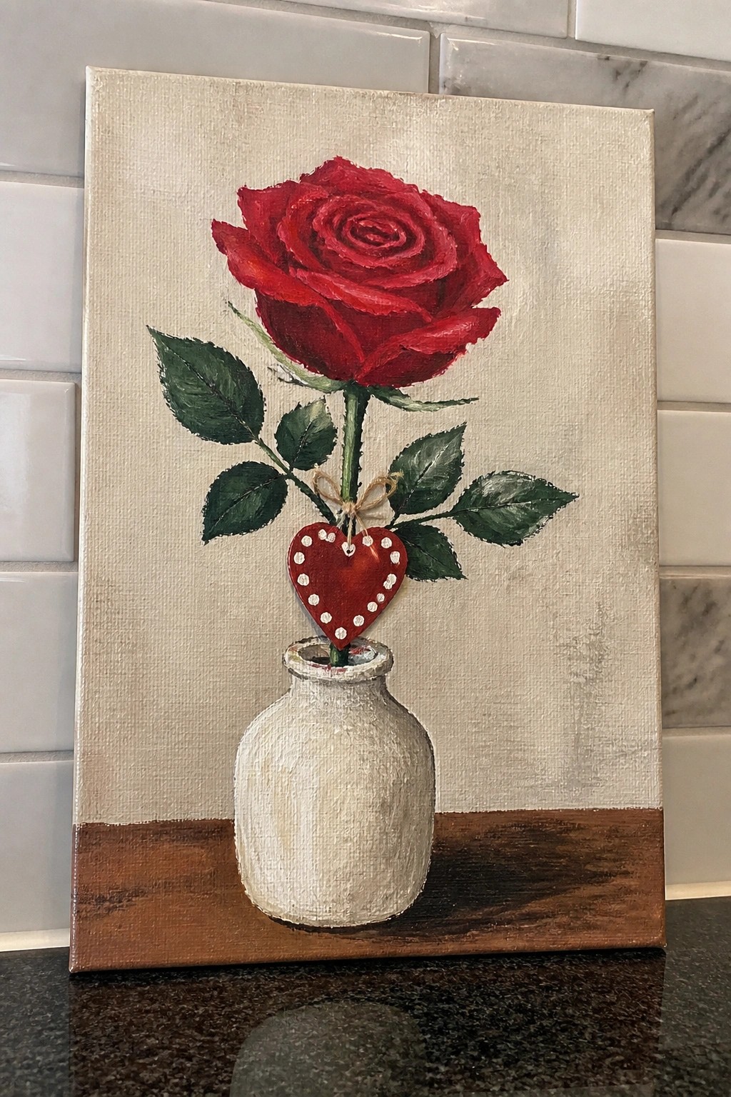 Red rose in white vase with red heart ornament on wooden surface