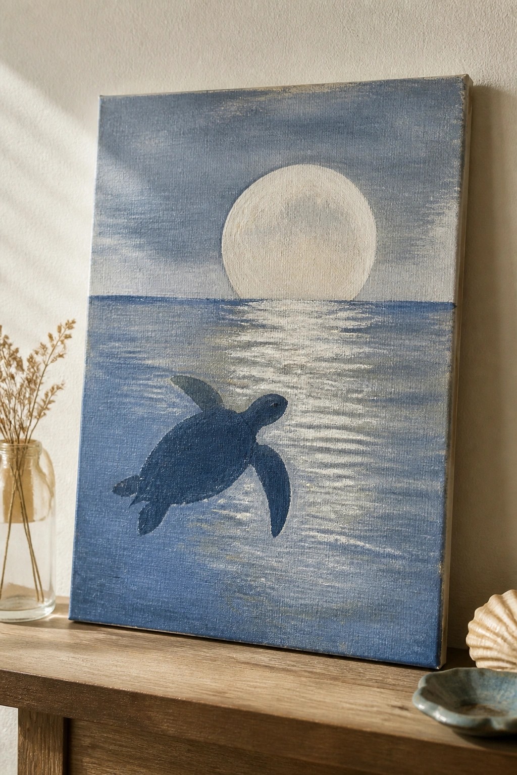 Blue painting of sea turtle swimming under moon on wooden shelf with shell