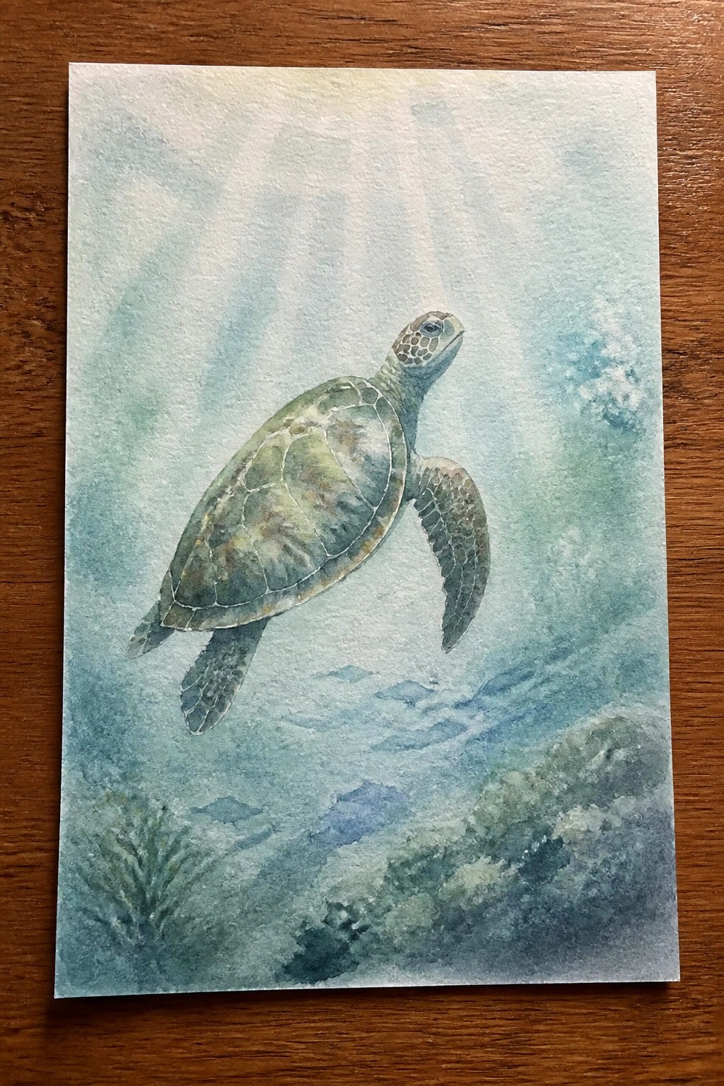 A watercolor painting of a sea turtle swimming underwater with light rays from above and small fish near the seabed.