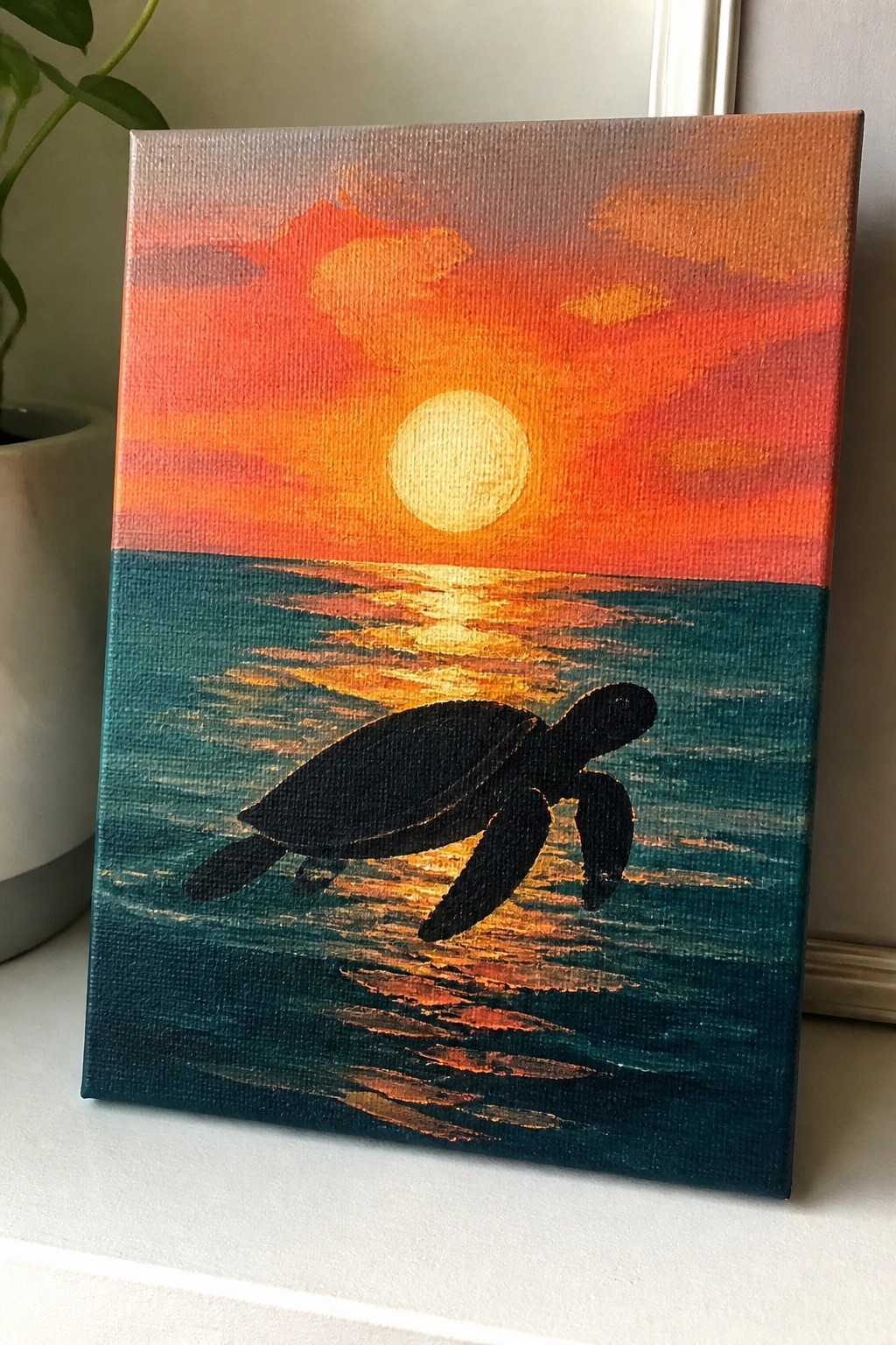 Silhouetted sea turtle in teal ocean with golden sunset reflections and orange sky