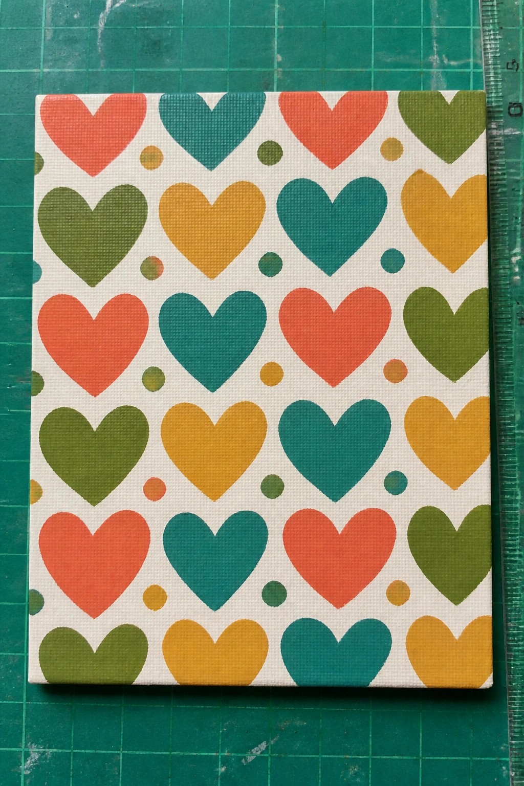 Canvas with colorful hearts in red teal orange green yellow on green cutting mat
