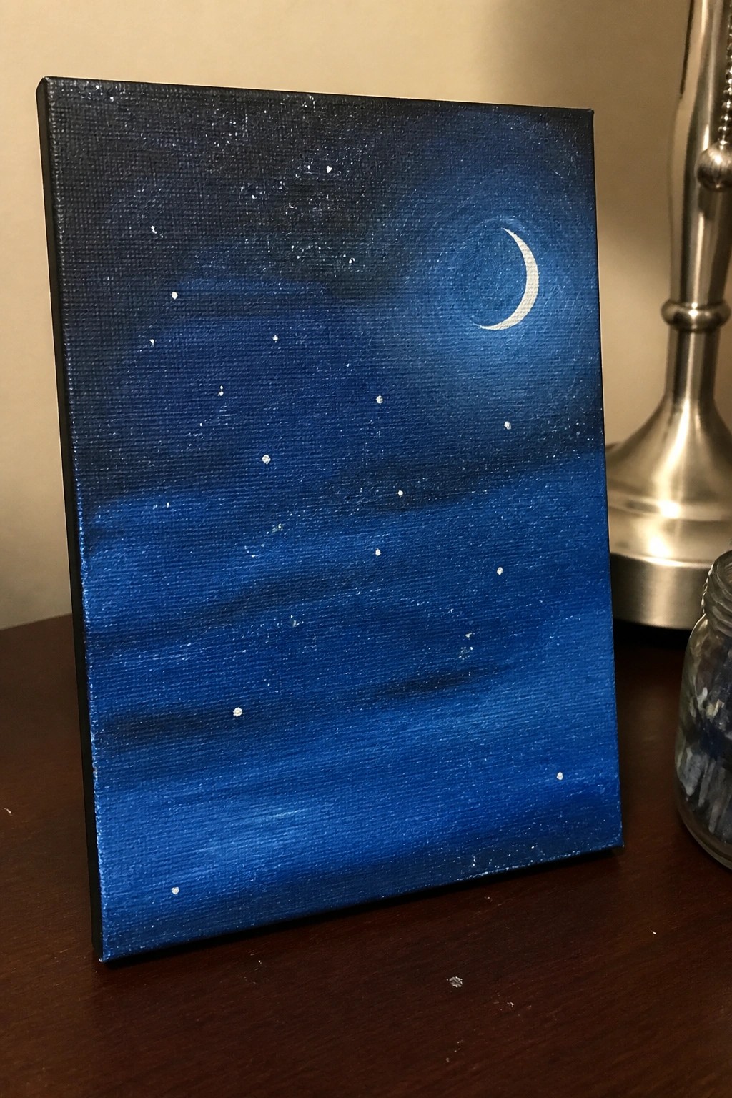 Blue night sky canvas painting with crescent moon and stars on wooden table
