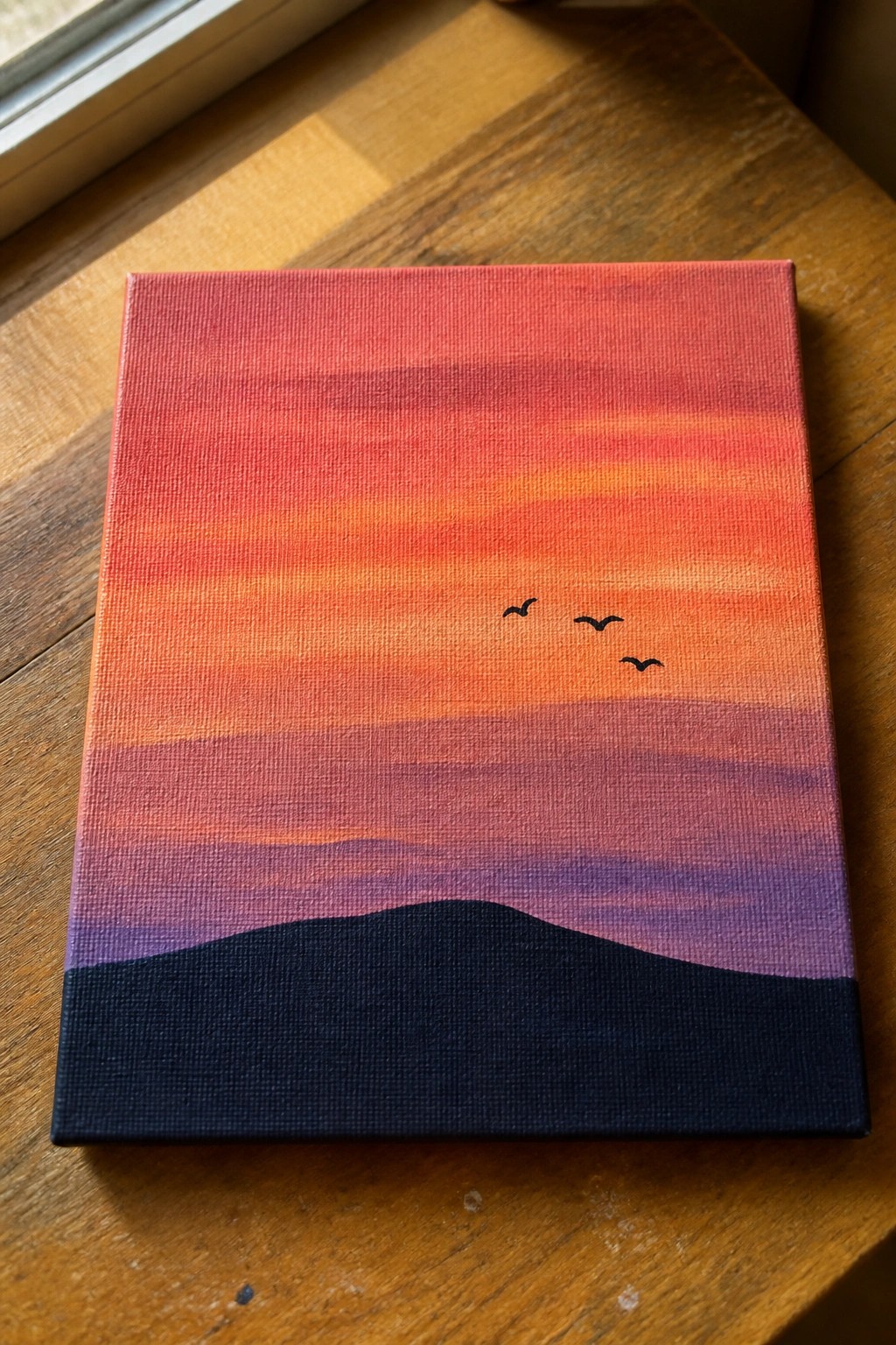Gradient sunset painting on canvas with red-orange sky, purple hills, black silhouette and birds