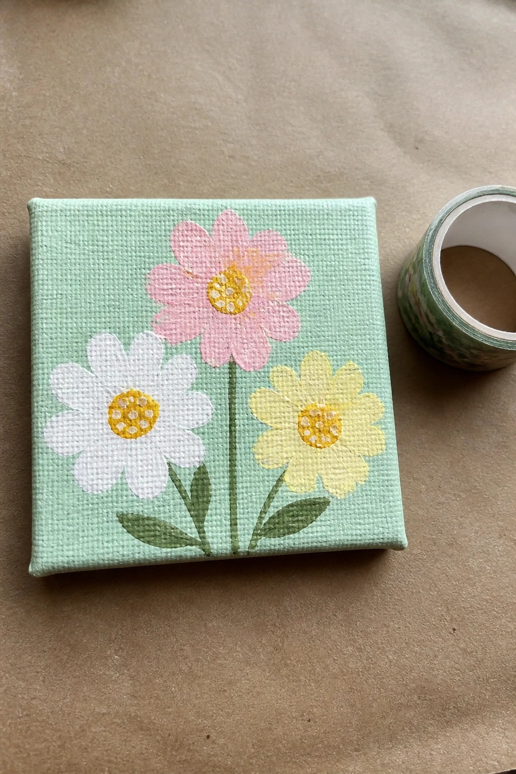 Small canvas with pink, white, and yellow flowers on light green background beside tape roll