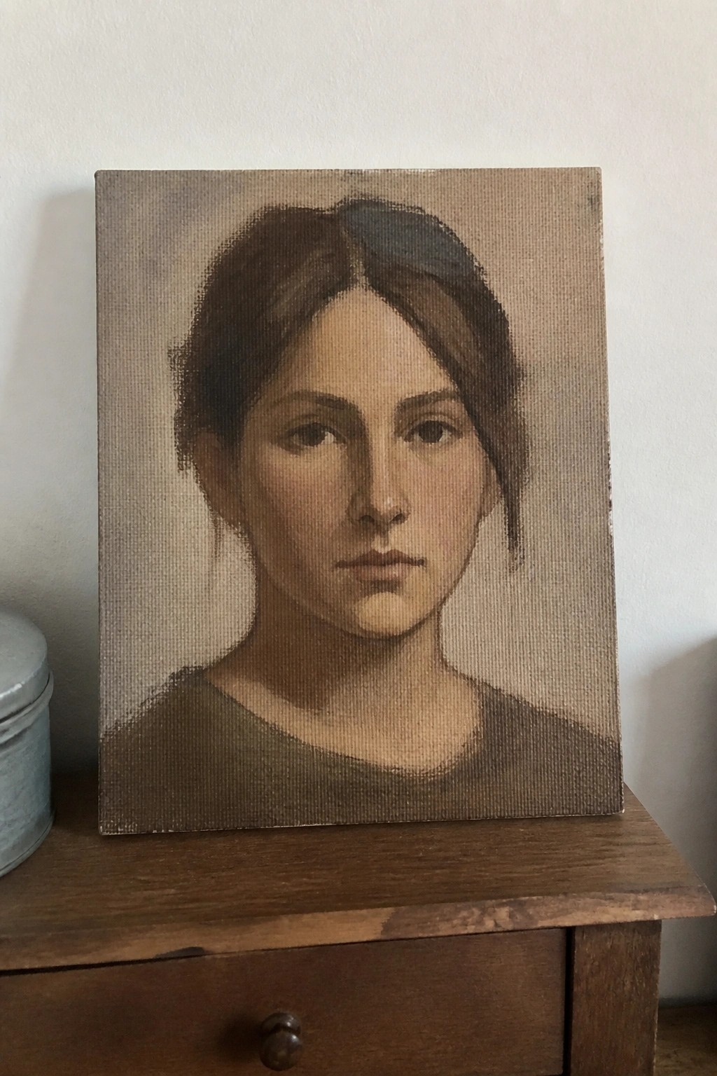 Painted portrait of a woman with brown hair on wooden dresser next to tin