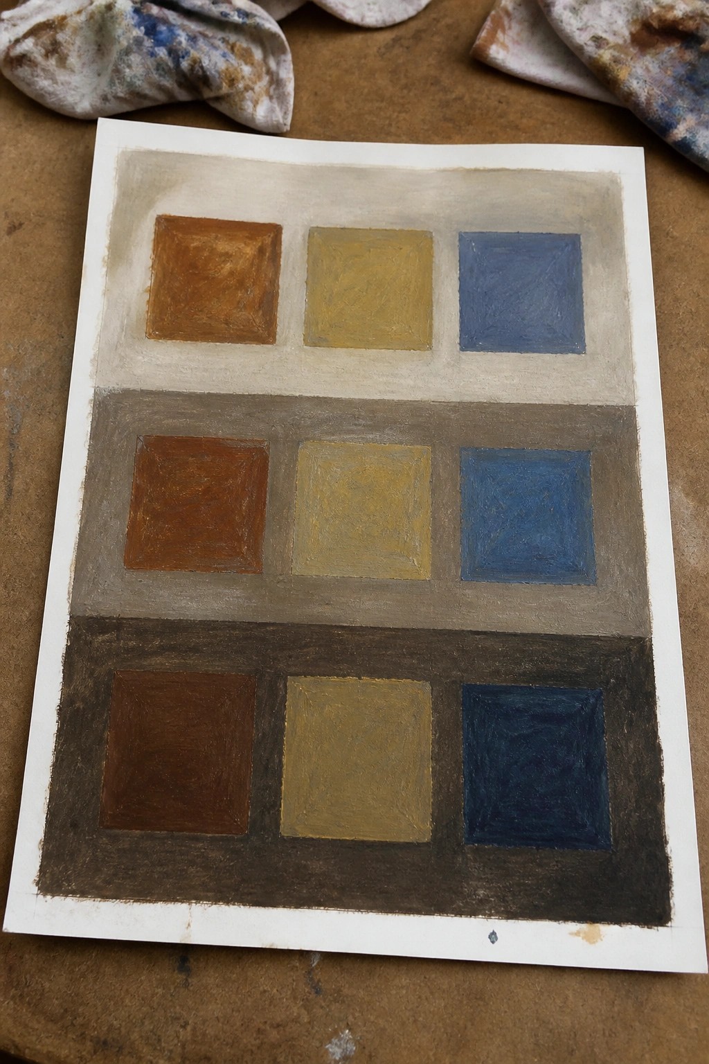 Three-tiered color study with brown, yellow, blue squares on beige, gray, brown backgrounds and rags.