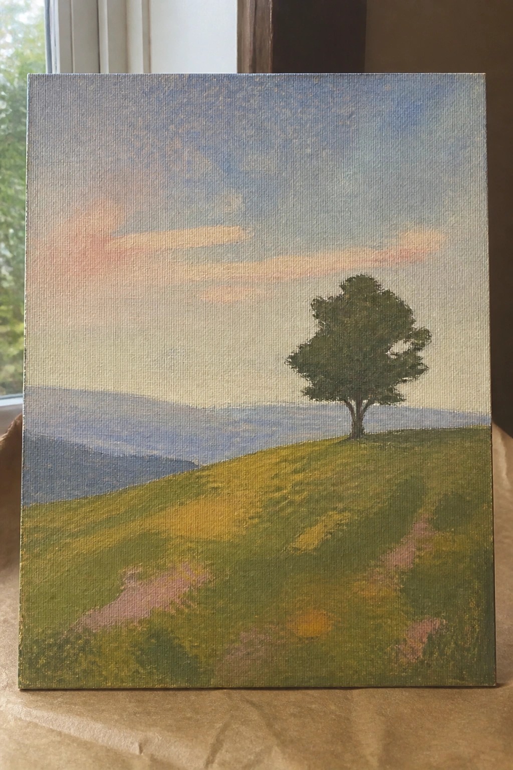 Lone tree on grassy hillside with distant mountains under pink and blue sky