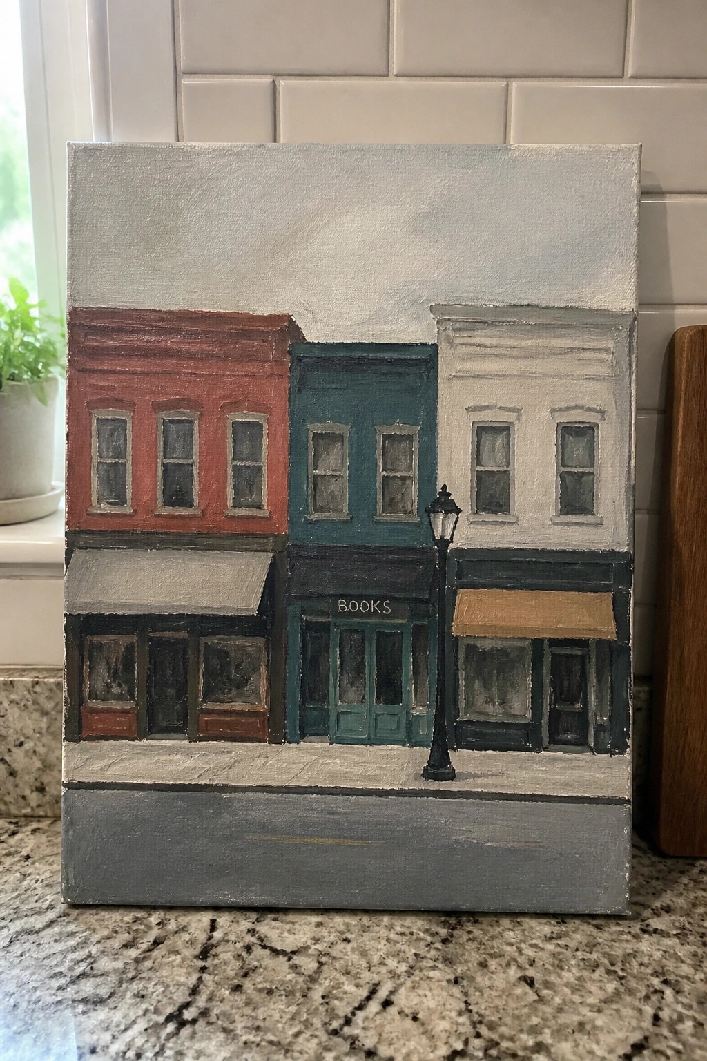 Colorful painting of red, teal, and white storefronts with books sign and lamppost