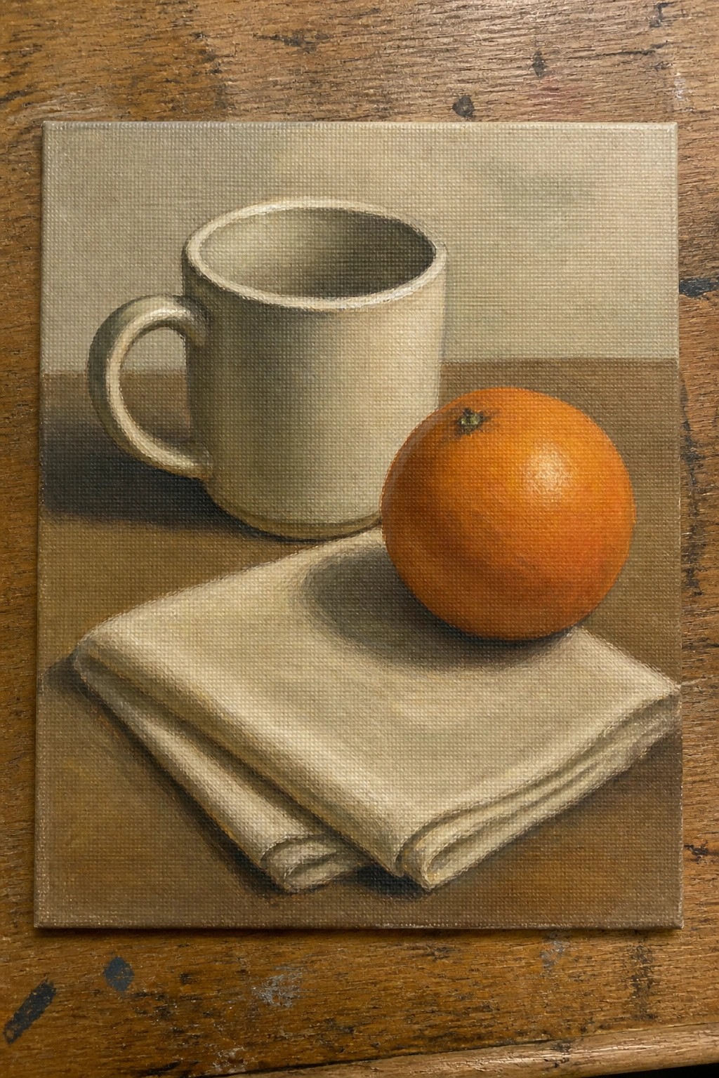 Still life painting of white mug, orange, and folded cloth on brown surface