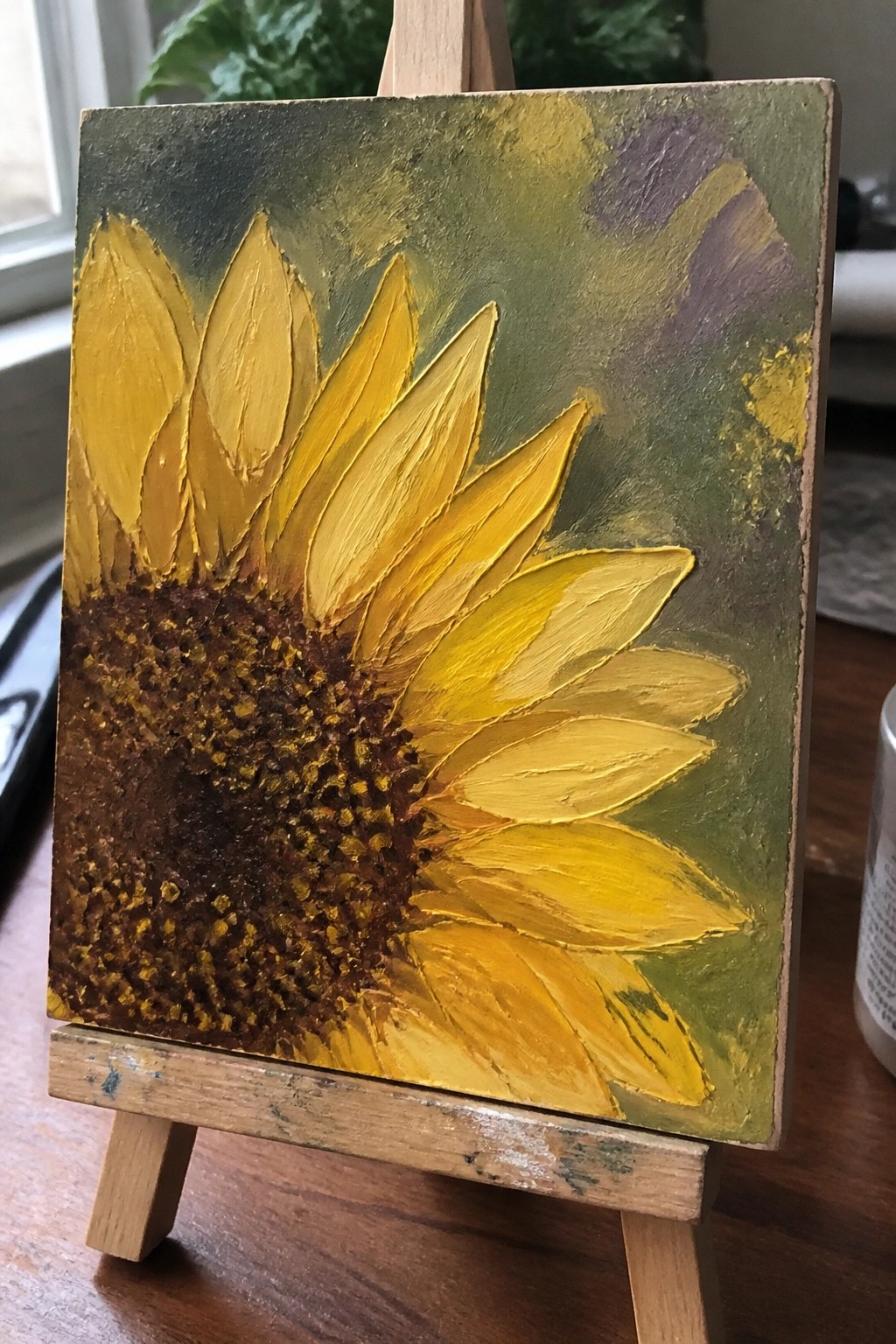 Vibrant yellow sunflower painting with textured brown center on small wooden easel.
