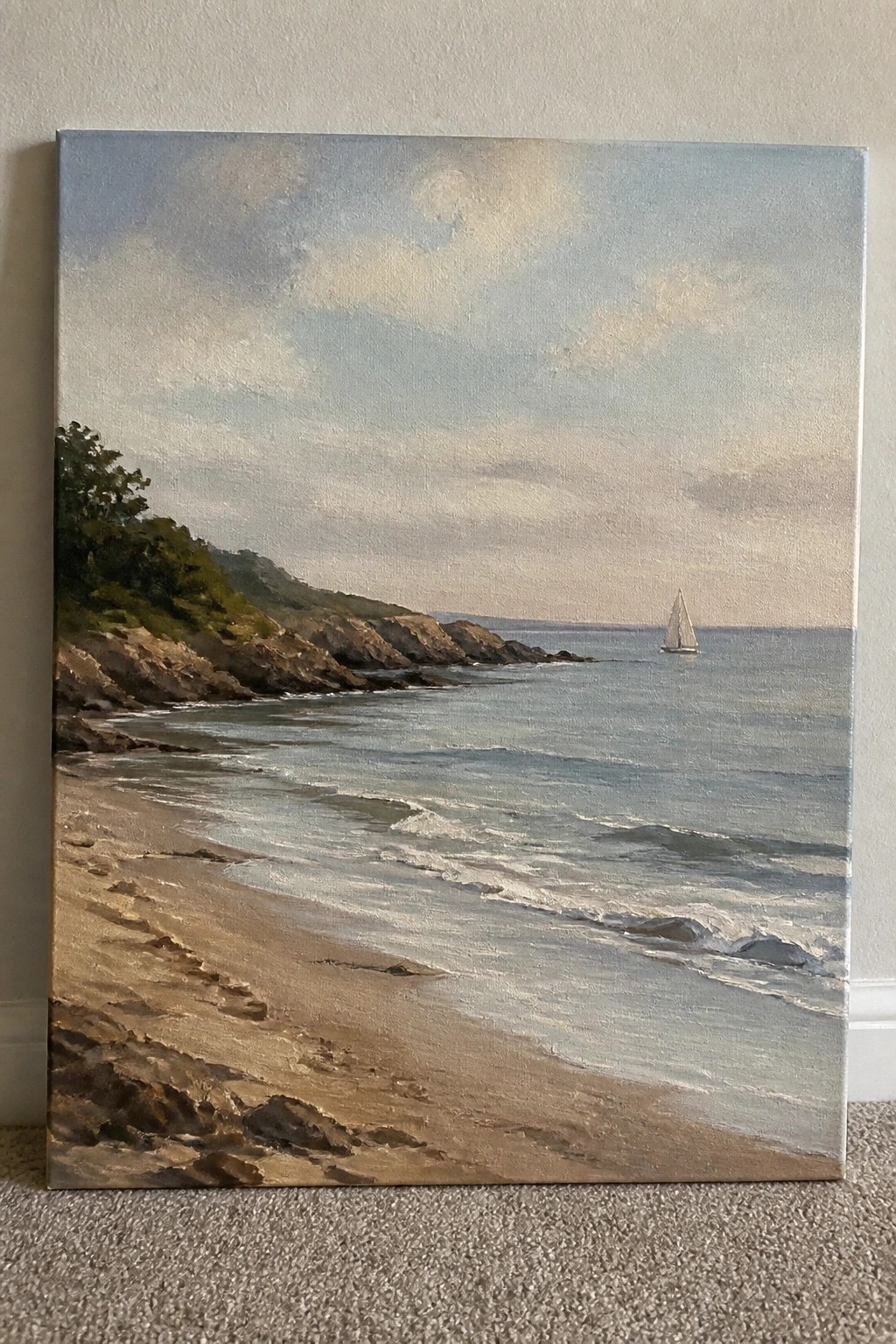 Realistic seascape painting of sandy beach with footprints, waves, cliffs, and distant sailboat.