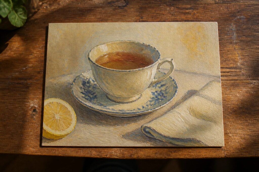 Still life painting of teacup with tea, half lemon, and napkin on wooden table
