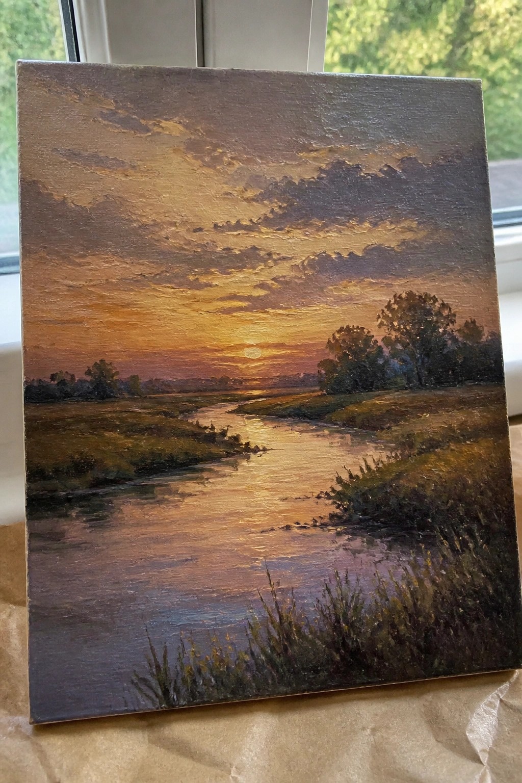 Sunset landscape painting with orange sky, winding river, grassy fields, and trees.