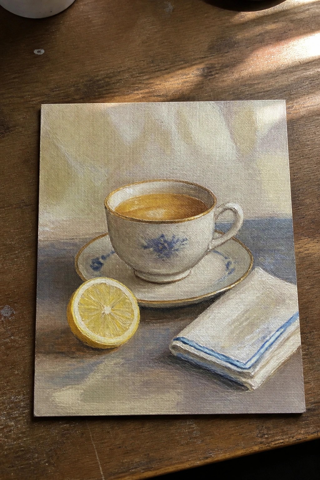 Still life painting of teacup with tea, half lemon, and napkin on wooden table