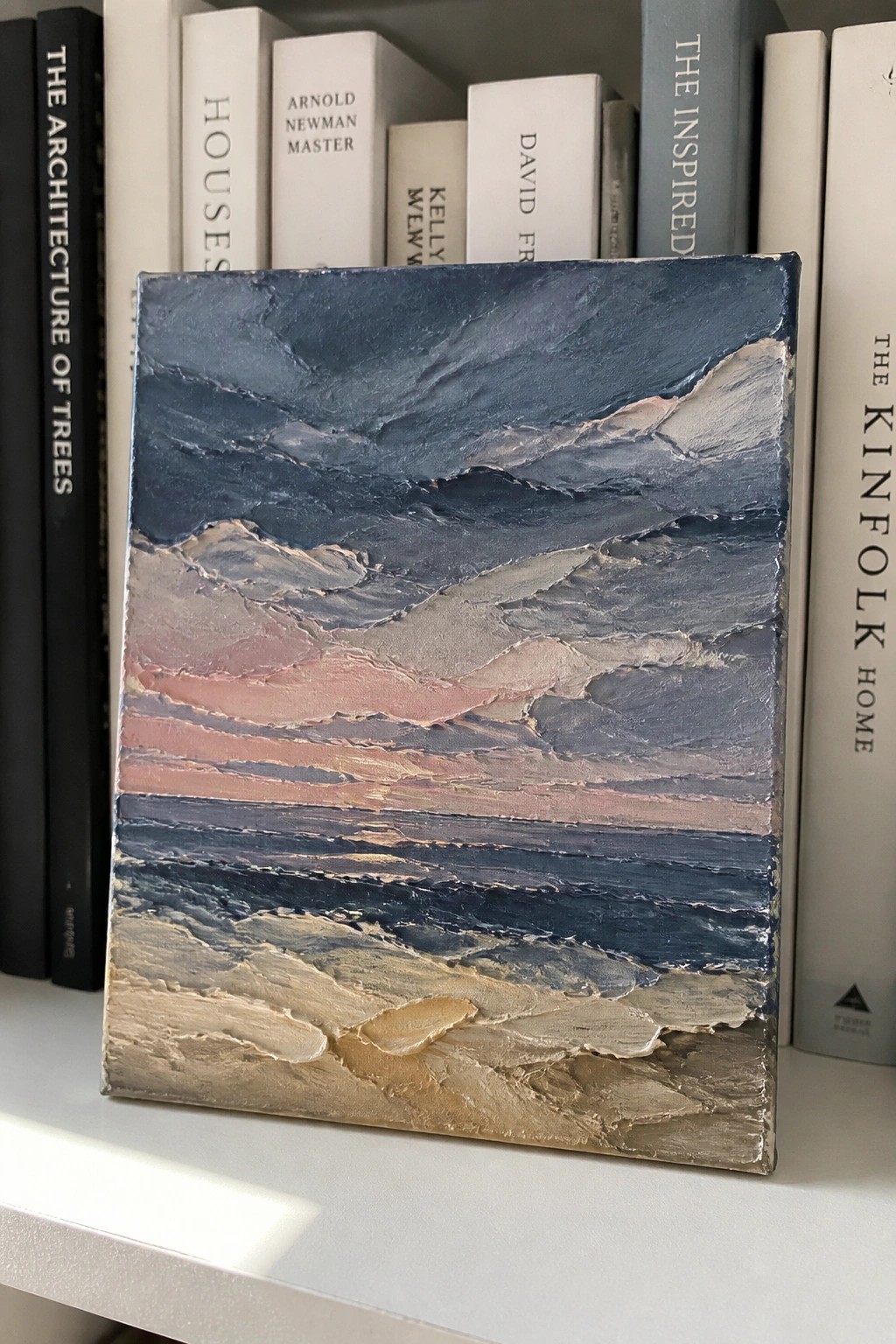 Textured abstract painting with blue, pink, and beige layers against books on shelf