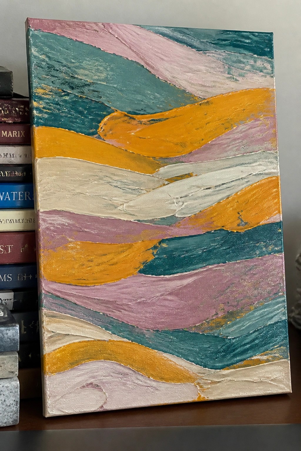 Abstract painting with thick wavy stripes in teal, pink, orange, white, and purple beside books.