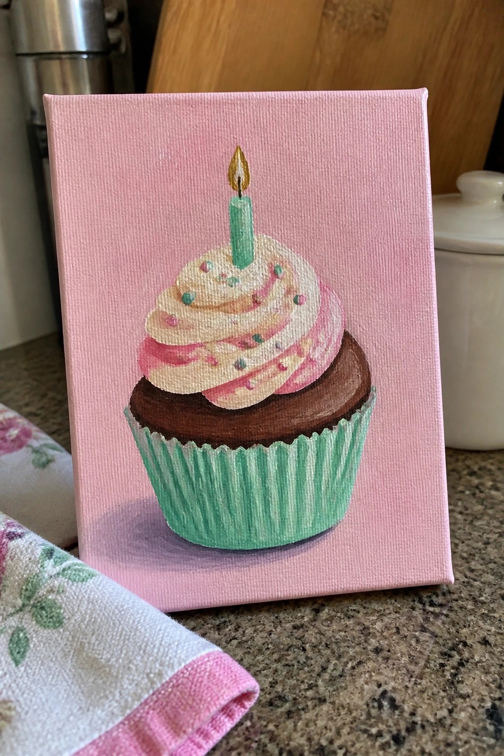 Hand-painted cupcake on pink canvas with chocolate base, pink frosting, and green candle