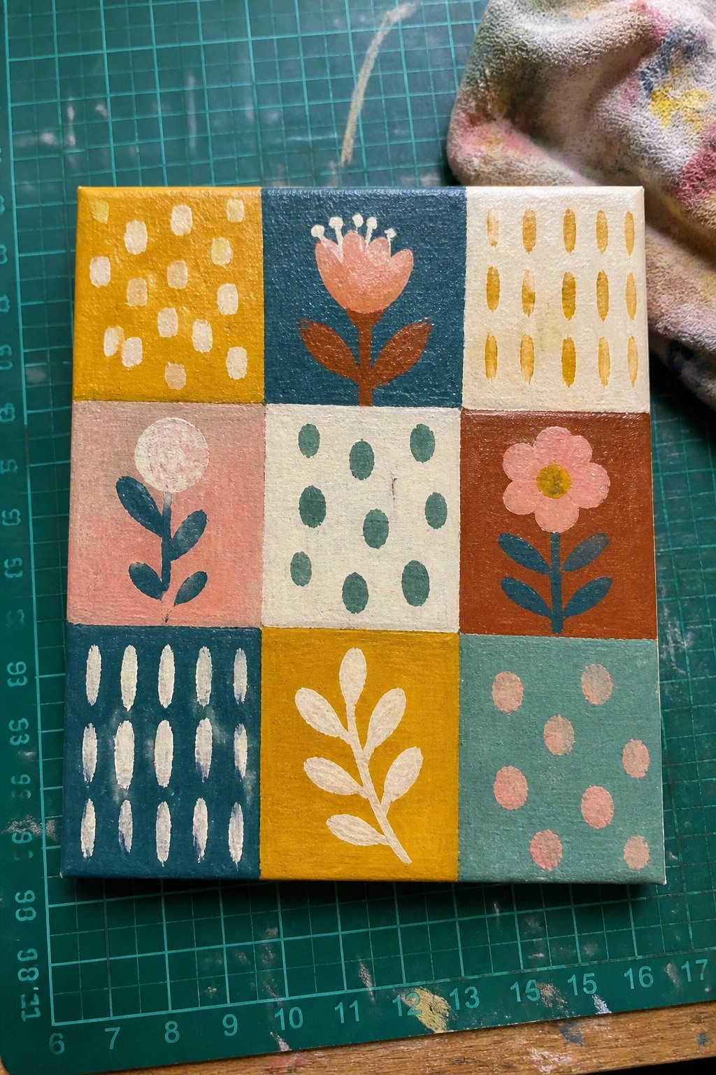 Vibrant hand-painted canvas with nine colorful sections of flowers, leaves, and dots.