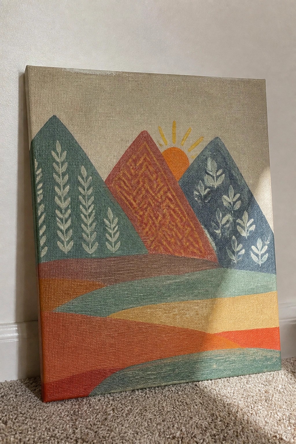 Abstract canvas painting of patterned mountains and sun leaning against wall on carpet