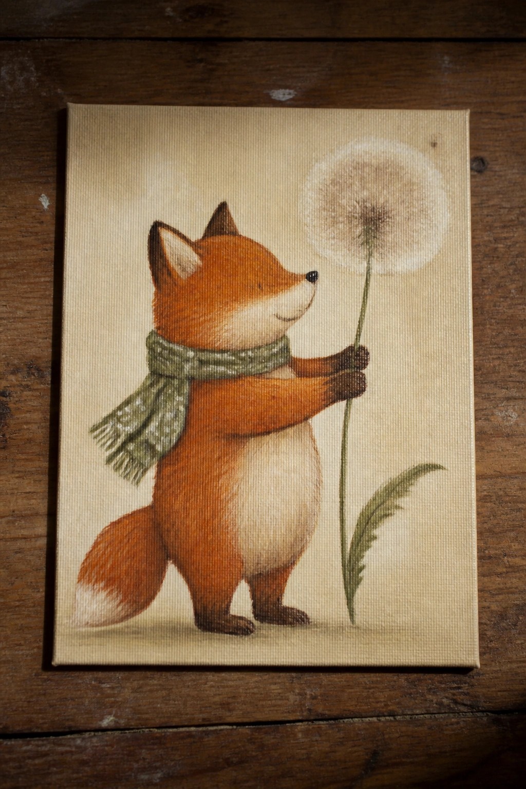 Orange fox in green scarf holds large fluffy dandelion on canvas.