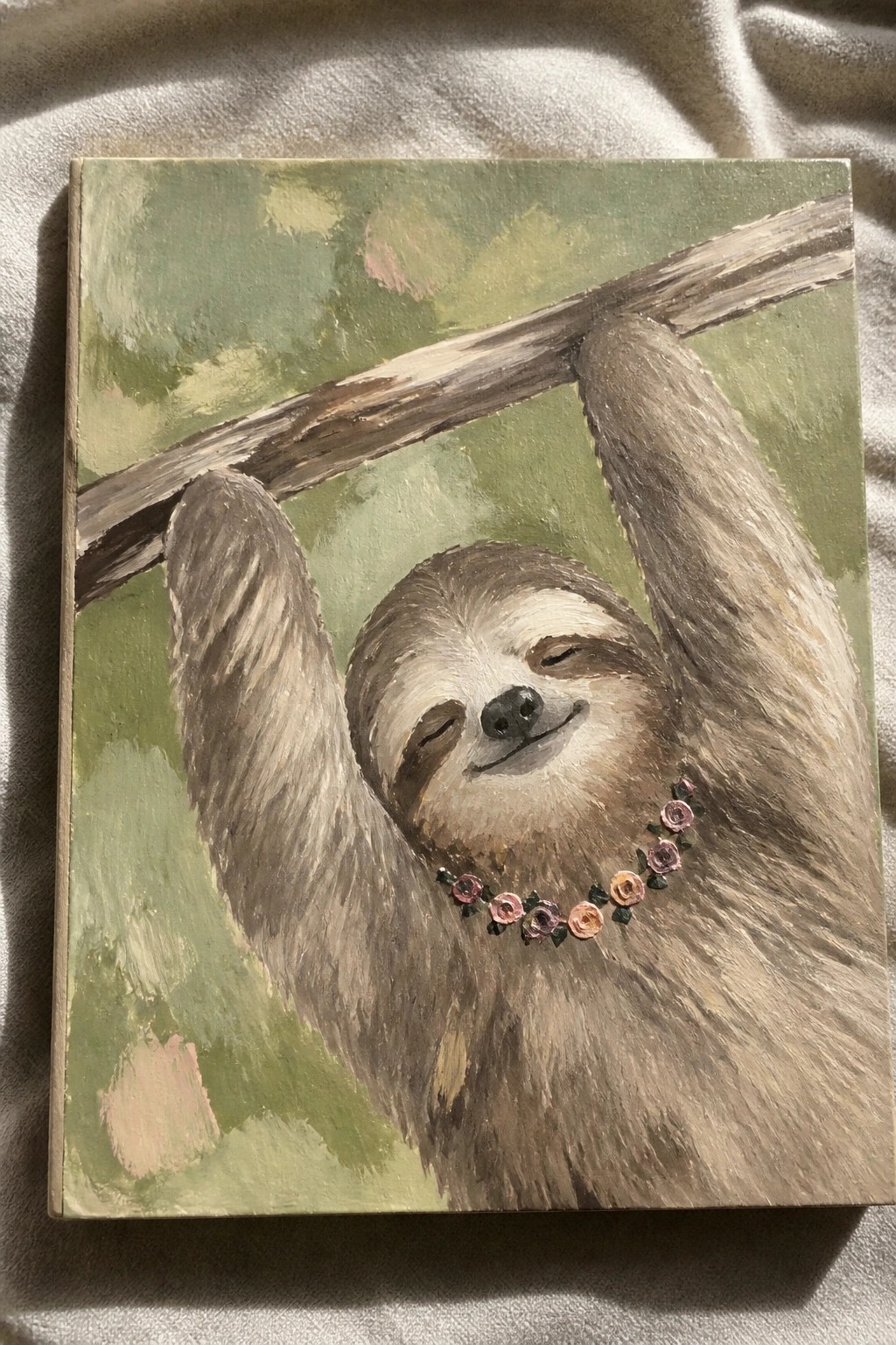 Smiling sloth with pink flower garland hangs from tree branch in green painting.