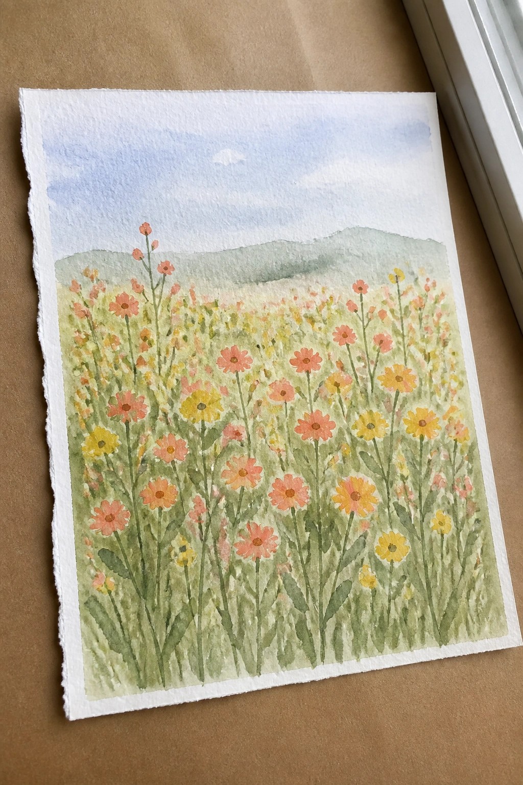A watercolor painting of a field of pink, orange, and yellow wildflowers with green stems in front of layered green hills under a blue sky.