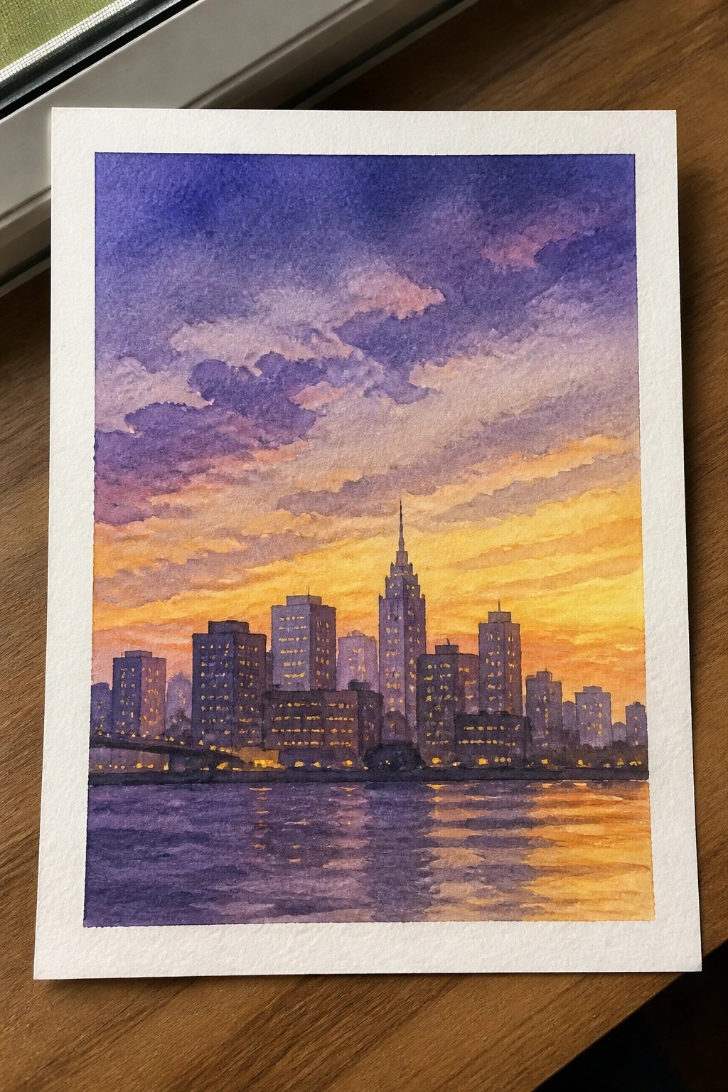 Watercolor city skyline at sunset with glowing windows reflected in purple water