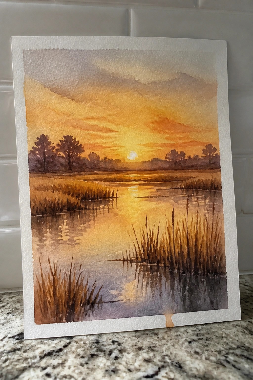 Watercolor sunset over marsh with orange sky, silhouetted trees, reeds, and glowing reflections.