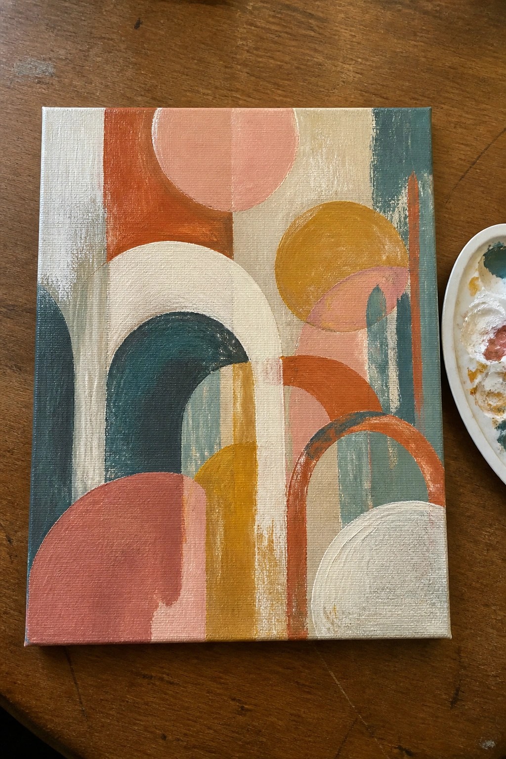 Abstract painting with colorful circles, arches, and stripes on canvas beside palette